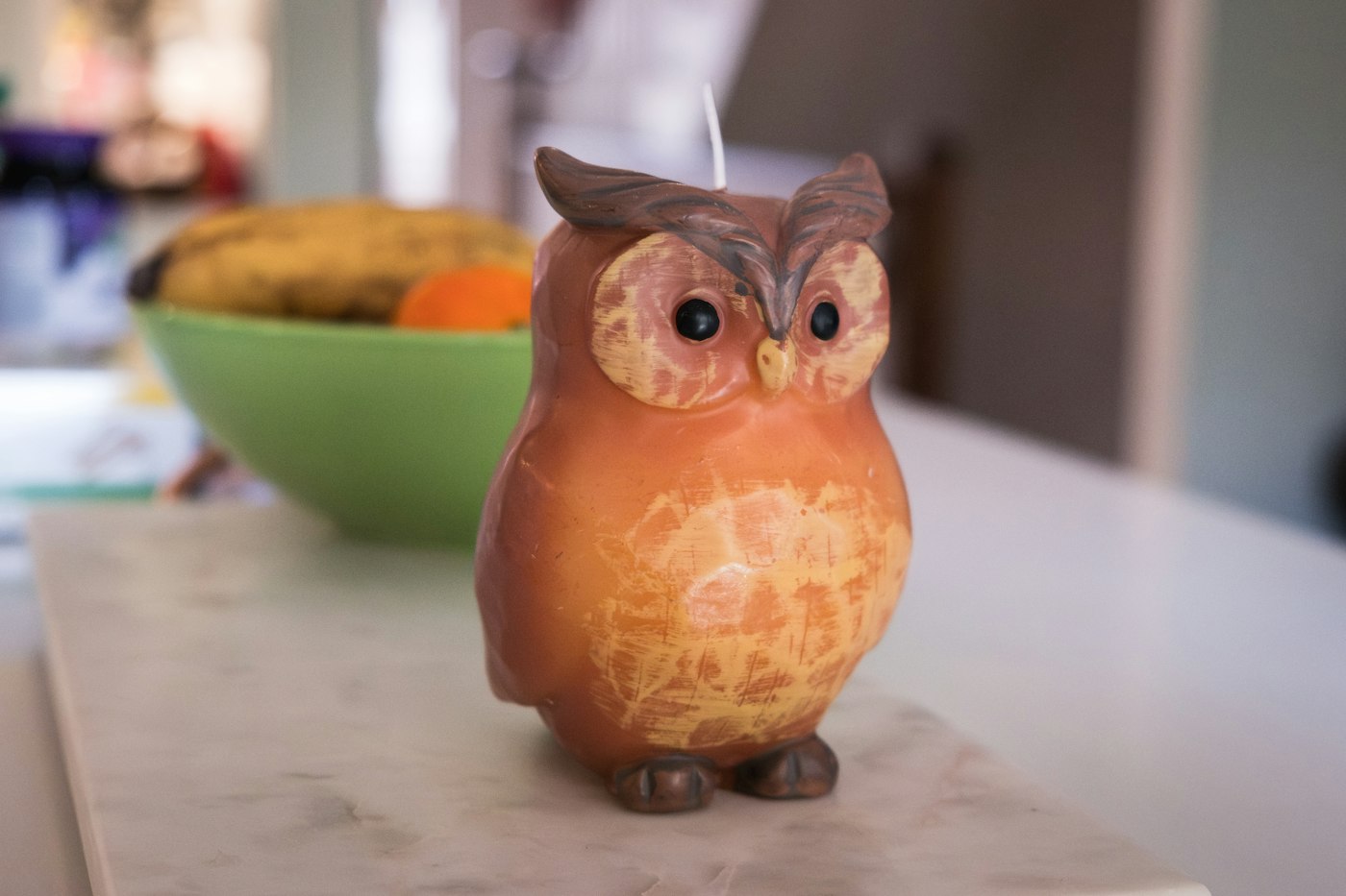 An owl-shaped candle sits on a marble surface.